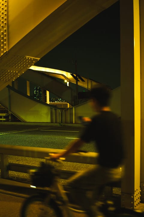 A blurred cyclist passing in front of a bridge lit in yellow