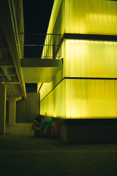 A person playing a piano beneath a glowing yellow building
