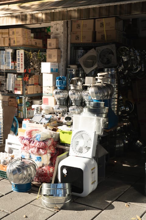 Metal ventilators and goods stacked outside a sunlit shop