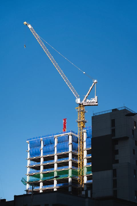 A yellow crane and a building under construction against blue sky