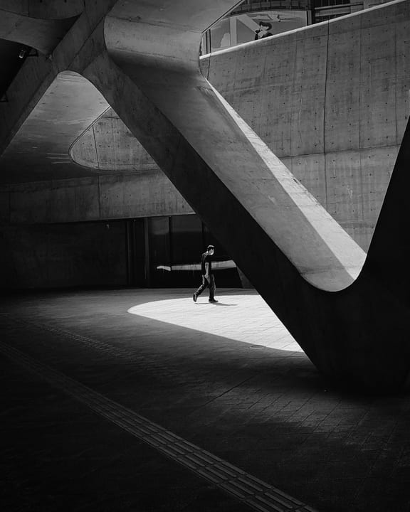 A person walking through sunlight beneath curved concrete in black and white