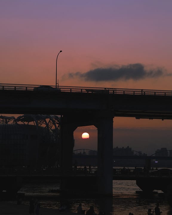The setting sun between bridge pillars and silhouettes along the river