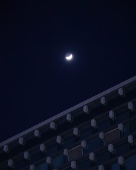 A crescent moon in the night sky above a dark building