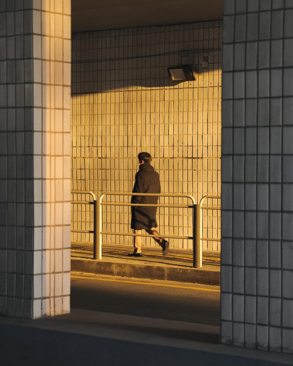 A person walking through golden sunlight between tiled pillars